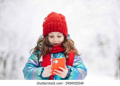 Happy Little Kid Use Smart Phone Funny Face Mask App Look At Cell Screen Smiles At Something Funny. Holidays And Celebrations Concept. The Dead Of Winter, Cold Weather, Frost, Snow