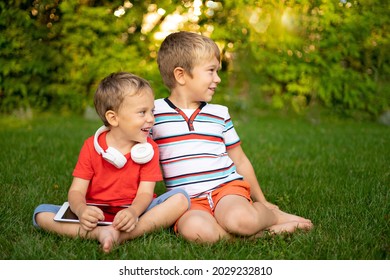 Happy Little Kids Boys In Wireless Headphones Hold A Tablet Computer Outdoors In A Summer Park, Smile, Communicate, Children's Interaction