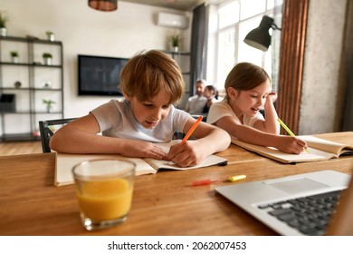 Happy little kids brother sister at table at home handwrite write do homework for school together. Small smart teen children study learn online on computer. Homeschooling, distant education.