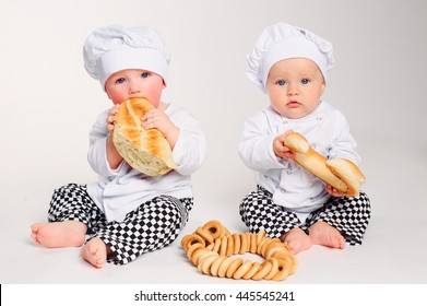 Happy little kids with chef hats eating fresh bread and pastry. Studio shot.