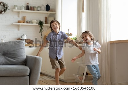 Happy little preschooler siblings have fun run around kitchen together, smiling small brother and sister feel playful racing playing engaged in funny childish activity at home, entertainment concept