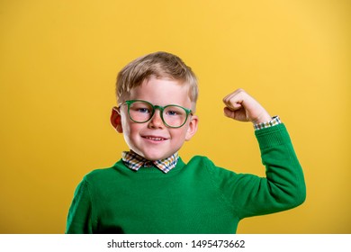 Happy little school boy showing bicep muscles. School boy in glasses isolated on yellow background. Back to school.  Child with confidence  ready to defense from bullying