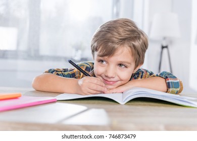 happy little schoolboy doing homework and writing in notebook - Powered by Shutterstock