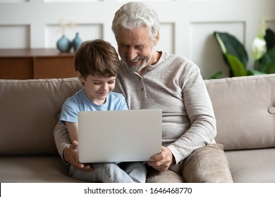 Happy little schoolboy relaxing on couch with smiling hoary senior old grandfather, using computer together. Friendly pleasant middle aged man cuddling small grandson, playing online game, shopping. - Shutterstock ID 1646468770