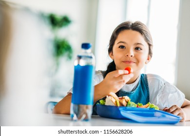 Happy Little Schoolgirl Eating Lunch At School Cafeteria