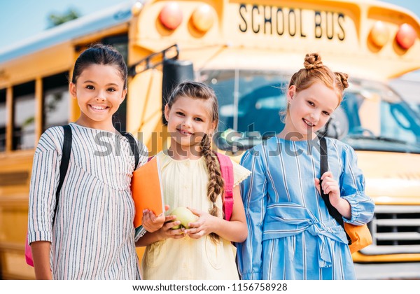 happy little schoolgirls looking at camera in front\
of school bus