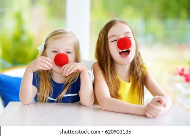 Happy little sisters wearing red clown noses having fun together on sunny summer day at home. Two kid playing together.