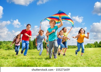 Happy little smiling boy with kite running in the park with kite and group of friends in the park on sunny summer day - Powered by Shutterstock