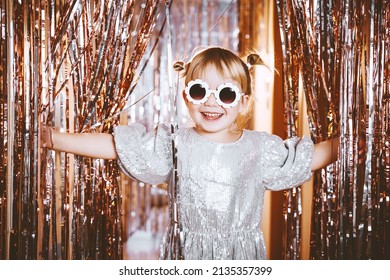 Happy little stylish girl in shiny dress having fun. Festive background with foil curtain decorations for kids birthday or fancy dress party, disco music or New Year. Celebration and Holiday concept. - Shutterstock ID 2135357399