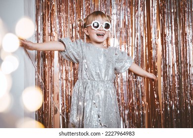 Happy little stylish girl in shiny dress having fun. Festive background with foil curtain decorations for kids birthday or fancy dress party, disco music or New Year. Celebration and Holiday concept. - Powered by Shutterstock