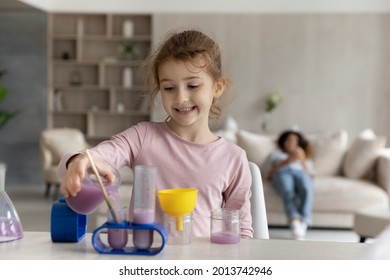 Happy little teen ethnic girl child have fun engaged in chemistry lab activity at home alone. Smiling small biracial teenage kid play laboratory game on table, make experiments feel playful.