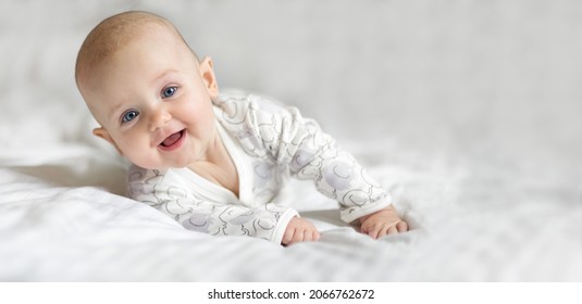 Happy little toddler baby girl smiling lying on the bed on a white sheet at home looking at the camera. Copy space for text, mock up, banner