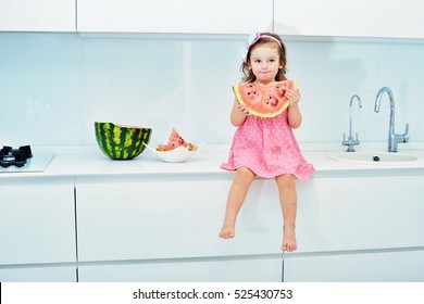 Happy little toddler girl eating fresh ripe watermelon for healthy breakfast in a white sunny family kitchen. Baby on the table at home. - Powered by Shutterstock