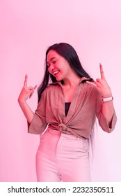 A happy and lively young asian woman partying. Posing behind a plain background with hot pink neon effect. - Shutterstock ID 2232350511