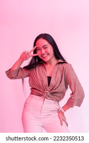 A happy and lively young asian woman partying. Posing behind a plain background with hot pink neon effect. - Shutterstock ID 2232350513