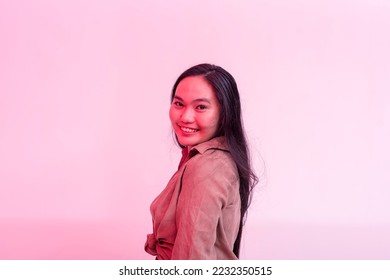 A happy and lively young asian woman posing behind a plain background with hot pink neon effect. - Shutterstock ID 2232350515