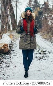Happy lonely attractive young beautiful girl in warm clothing with backpack walking in forest or park. Single woman loves to walk alone on snow covered trail through trees. Enjoying fresh air. Hiking
