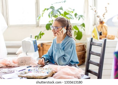 happy long-haired beautiful fashionable designer holding smartphone in hands talking with seamstress about chosen fabric, sitting at office - Shutterstock ID 1333613180