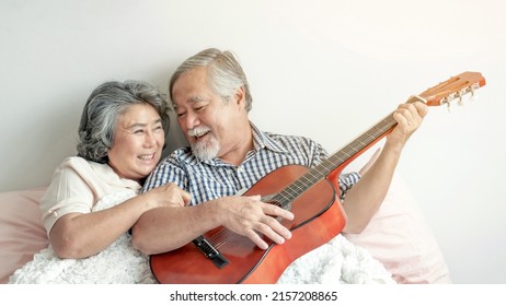 Happy Love Elderly Couple Smile Face, Senior Couple Old Man And Senior Woman Relax Playing Acoustic Guitar In Bed Room - Lifestyle Senior Concept 