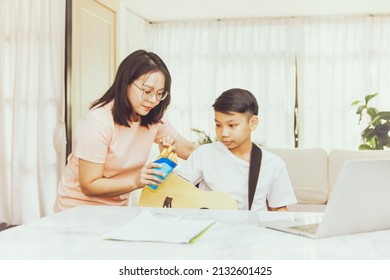 Happy Love Family And Affectionate Mother Feeds Her Son A Snack Or Snack While The Son Sits At Home Taking Online Guitar Lessons : Parenting And Coexistence Of Asian Families.