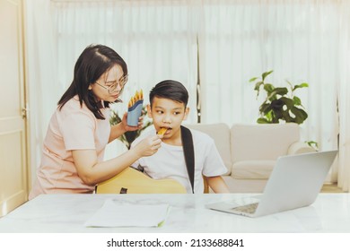 Happy Love Family And Affectionate Mother Feeds Her Son A Snack Or Snack While The Son Sits At Home Taking Online Guitar Lessons : Raising And Living In A Shared Home Asian Family.
