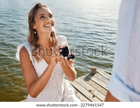 Happy, love and a woman proposing to a man, getting engaged and showing a ring. Couple, excited and a young girl asking her boyfriend for marriage, kneeling to propose and ask a question by a lake Foto stock © 