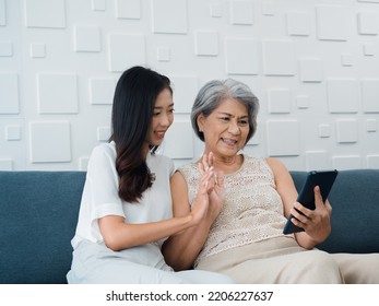 Happy Lovely Asian Senior Woman, Mother White Hair And Beautiful Young Female, Daughter Waving Greeting At Digital Tablet Screen While Sit On Couch In White Room. Meet Family By Video Call At Home.