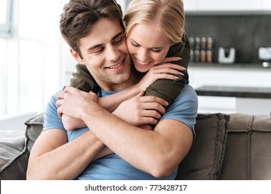 Happy lovely blonde woman hug with her husband while sitting on sofa at home - Shutterstock ID 773428717