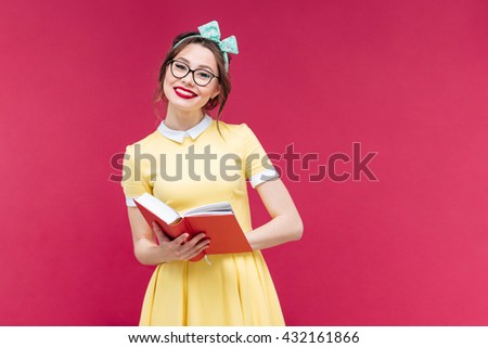 Happy lovely pinup girl in glasses reading a book over pink background