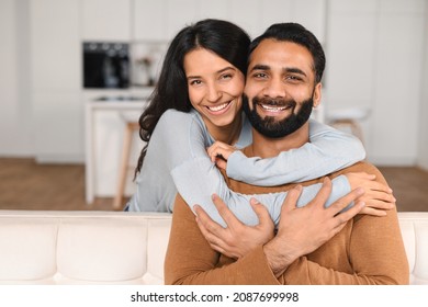 Happy lovely young Indian couple together at home, ethnic young wife hugging from behind her husband, sitting and resting on sofa in modern apartment, portrait of romantic multiracial couple in love - Shutterstock ID 2087699998