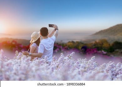 Happy lovers holding smart phone selfie photo at floral flowers park with nice land scape fog around nature background.