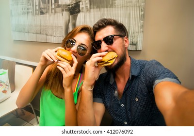 Happy Lovers,attractive Woman And Man Traveling In Tropical Island Enjoying Romance. Attractive Couple Making Selfie,smiling And Have Fun Together.Couple Eating Big Burgers,cheeseburger And Coke.fun