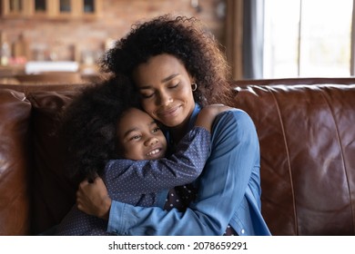 Happy loving African American little child girl cuddling young biracial mother, missing after long separation time, showing sweet tender feelings resting together on sofa at home, candid relations. - Powered by Shutterstock