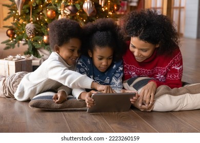 Happy loving African American mom and teen kids relax on New Year at home talk on video call on pad. Smiling biracial mother and children relax near fir tree on Christmas use tablet together. - Powered by Shutterstock