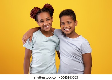 Happy loving black brother and sister teenagers hugging and smiling on yellow studio background, showing affection, wearing white t-shirts. Siblings, family, relationships concept