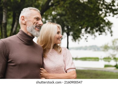 Happy loving caucasian mature husband and wife spouses couple looking at the same direction, hugging embracing together on a date in park.