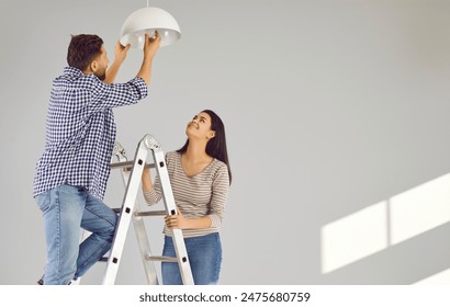 Happy loving couple changing light bulb in new apartment. Family moving in new apartment, doing DIY renovations at home. Cheerful husband and wife standing on ladder - Powered by Shutterstock