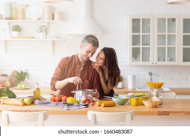 Happy loving couple cooking dinner together on kitchen. Young married man and woman preparing fresh organic vegetable. Husband surprising wife with culinary skill. Trendy loft home interior