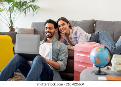 Happy loving couple planning trip after quarantine, buying low price tickets and booking hotel online, using laptop while sitting in living room with packed suitcases nearby - Powered by Shutterstock