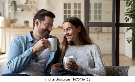 Happy loving couple relaxing on couch, drinking hot beverages, tea or coffee, holding white cups, smiling young man and woman chatting, talking, spending lazy weekend at home, sitting on cozy sofa - Powered by Shutterstock