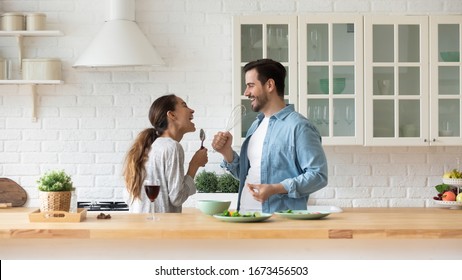 Happy loving couple singing song and dancing, having fun with kitchenware in kitchen, funny excited wife and husband holding whisk and spoon, listening to music, preparing food together - Powered by Shutterstock