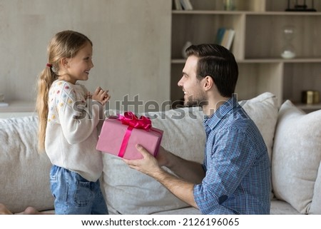 Happy loving dad giving surprise gift to excited little daughter kid, holding pink wrap, congratulating girl on birthday. Overjoyed child getting present from beloved daddy, feeling joy, happiness