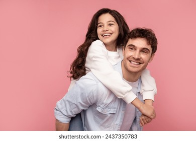 Happy loving daddy carrying daughter on back and both smiling, european family having fun on pink studio background, free space - Powered by Shutterstock