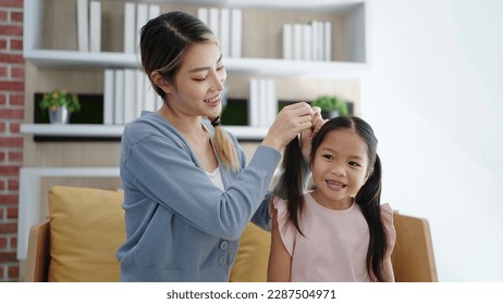 Happy loving family Asian mother is combing her daughter's braiding hair sitting on sofa at living room. Anti lice treatment - Powered by Shutterstock