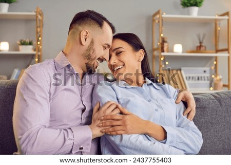 Happy and loving family couple shares a warm embrace on the sofa in the comfort of home. Smiles radiate happiness, capturing a beautiful moment of love, togetherness, and domestic bliss.