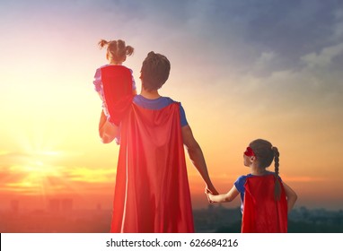 Happy loving family. Dad and his daughters are playing outdoors. Daddy and his children girls in an Superhero's costumes. Concept of Father's day.