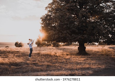 Happy Loving Family Father And Daughter Little Girl Playing Together Outdoors In Summer Sunset. Father's Day Concept Little Child Baby Hugs Dad Spending Weekend. Dad Tossing Up Throwing Baby In Air