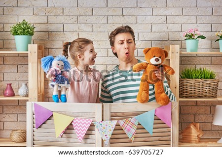 Happy loving family. Father and his daughter in kids room. Funny dad and lovely child having fun and playing performance in the puppet theater indoors. Doll and teddy bear.