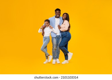 Happy Loving Family. Full Body Length Of Cheerful Black Man, Woman And Girl Standing Posing On Yellow Orange Studio Wall. Cheerful Guy Embracing Daughter And Wife, Teen Showing V Victory Sign, Banner