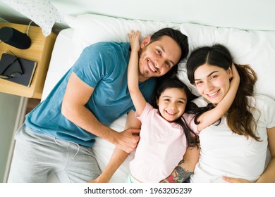 Happy Loving Family. Mom, Dad And Daughter Smiling And Making Eye Contact While Cuddling Together In Bed During A Relaxed Lazy Morning